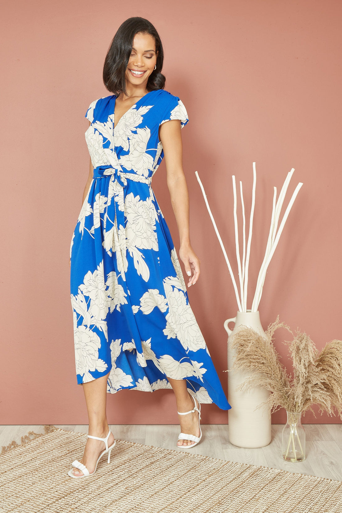 Yumi Blue Blossom Print Wrap Midi With Dipped Hem – flattering wrap-over midi dress in striking blue with pink blossom print, flowing dip hem below the knee, frill trim, cap sleeves and tie waist belt, 100% polyester, 119cm length
