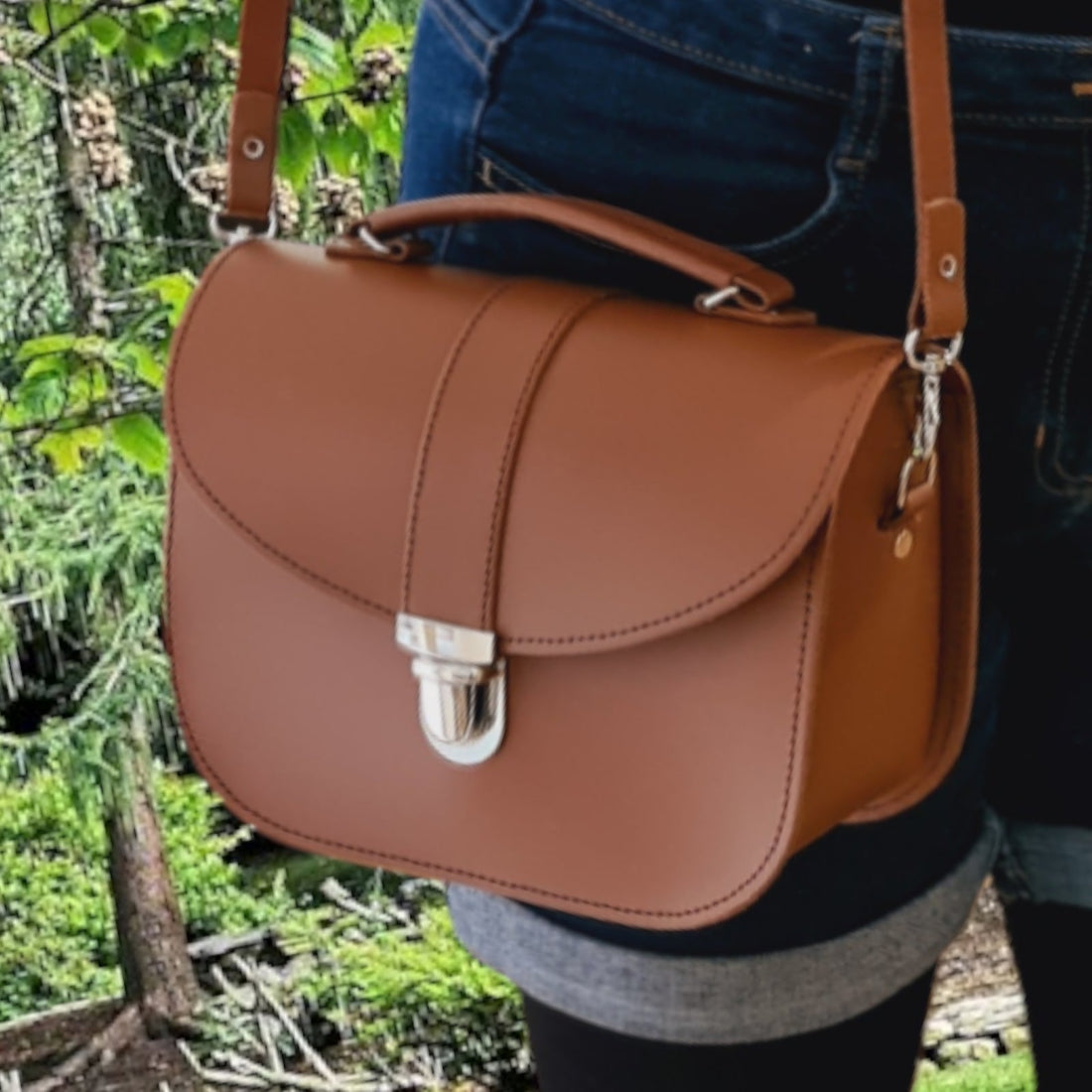 Woman carrying the Zatchels Olympia Handmade Leather Bag in Chestnut by the top grab handle, showing the warm chestnut leather tone, silver push-lock closure and classic structured silhouette