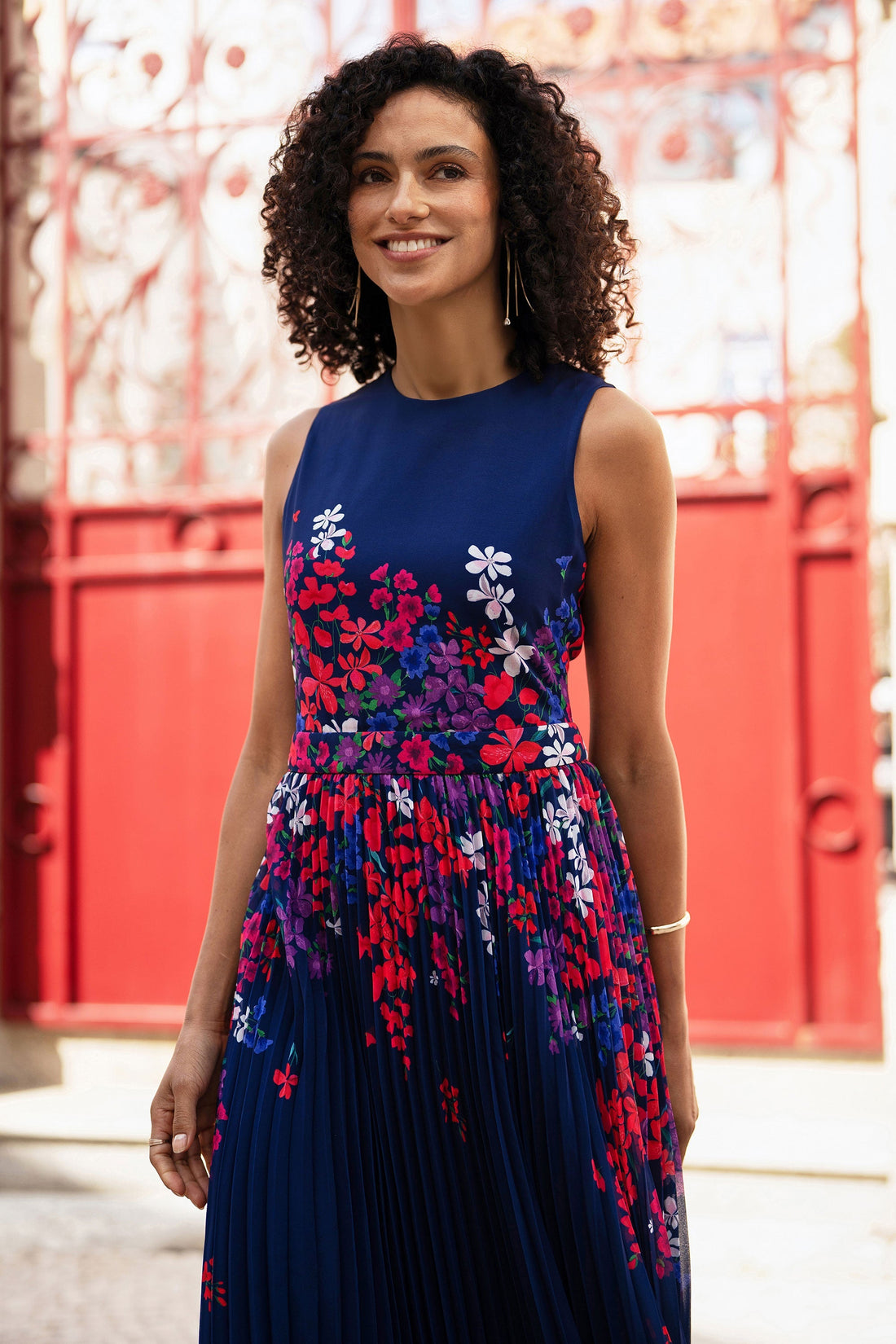 Yumi Navy Border Floral Print Midi Dress With Pleats — front view showing the sleeveless high-neck silhouette, the vibrant floral print cascading from the bodice into the flowing pleated midi skirt