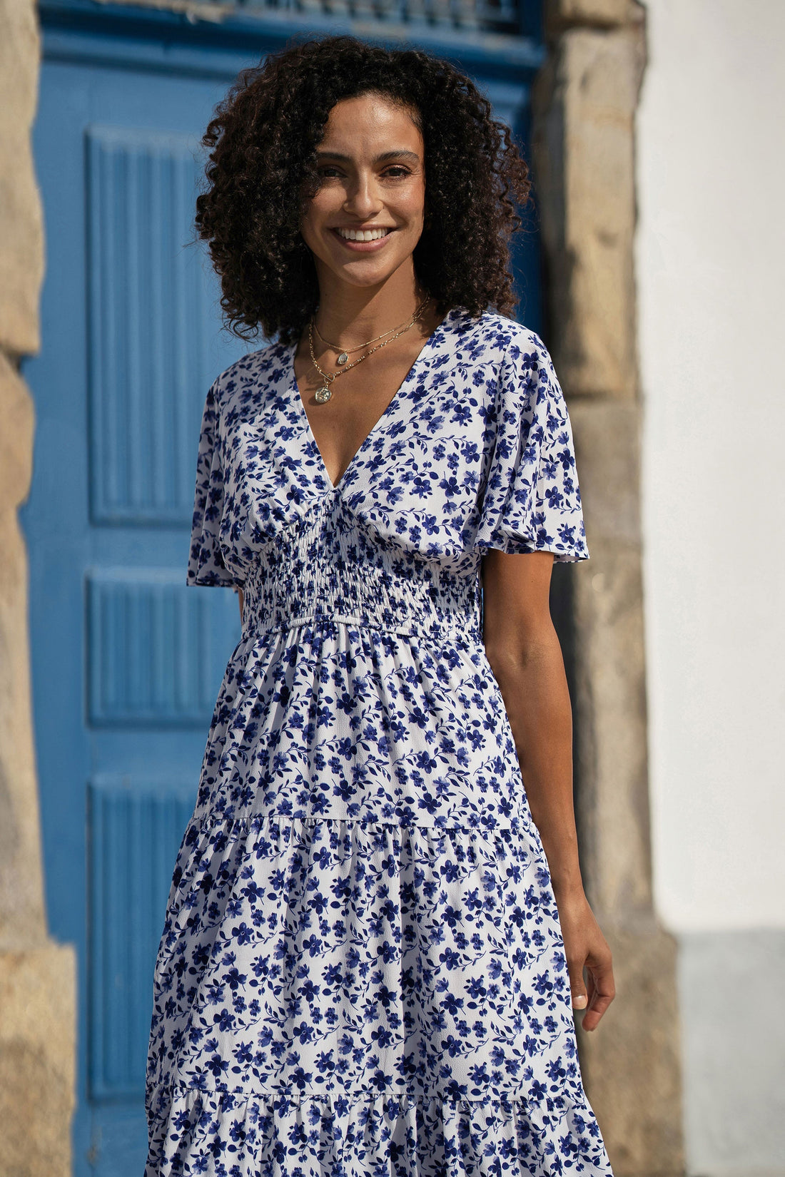 Yumi Blue Floral Ruched Waist Midi Dress with Angel Sleeves full length front view showing the V neckline flutter angel sleeves smocked waist blue and white floral print and flowing 116cm midi skirt