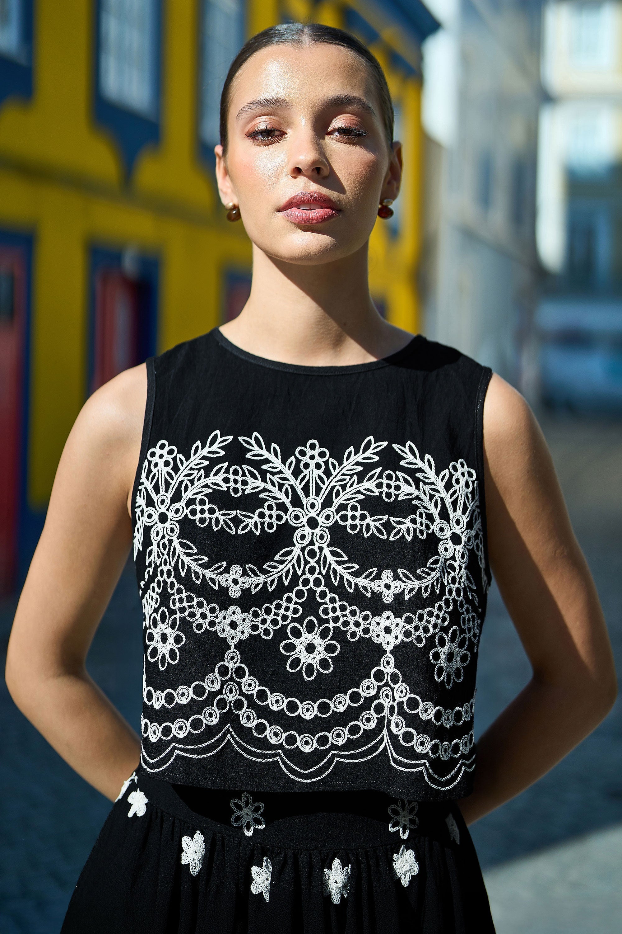 Yumi Black Embroidered Crop Top — front lifestyle view showing intricate white floral and scalloped embroidery on black sleeveless crop top, 44cm length with ornate lace-inspired detailing