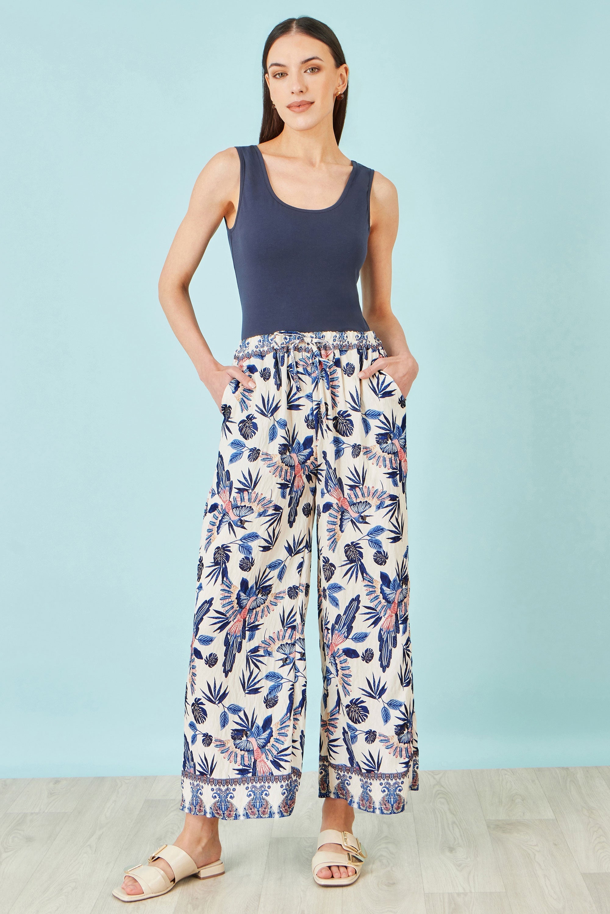 Yumi Blue Bird Print Viscose Wide Leg Trousers shown styled in a summer outfit displaying the tropical bird print, wide leg silhouette, decorative border hem and fluid viscose drape