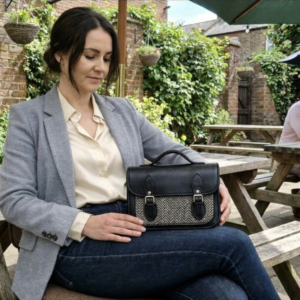 Woman wearing the Zatchels Midi Tannery and Tweed Satchel in Black crossbody showing the black tannery leather body, black and white heritage tweed front panel and silver nickel buckle detailing