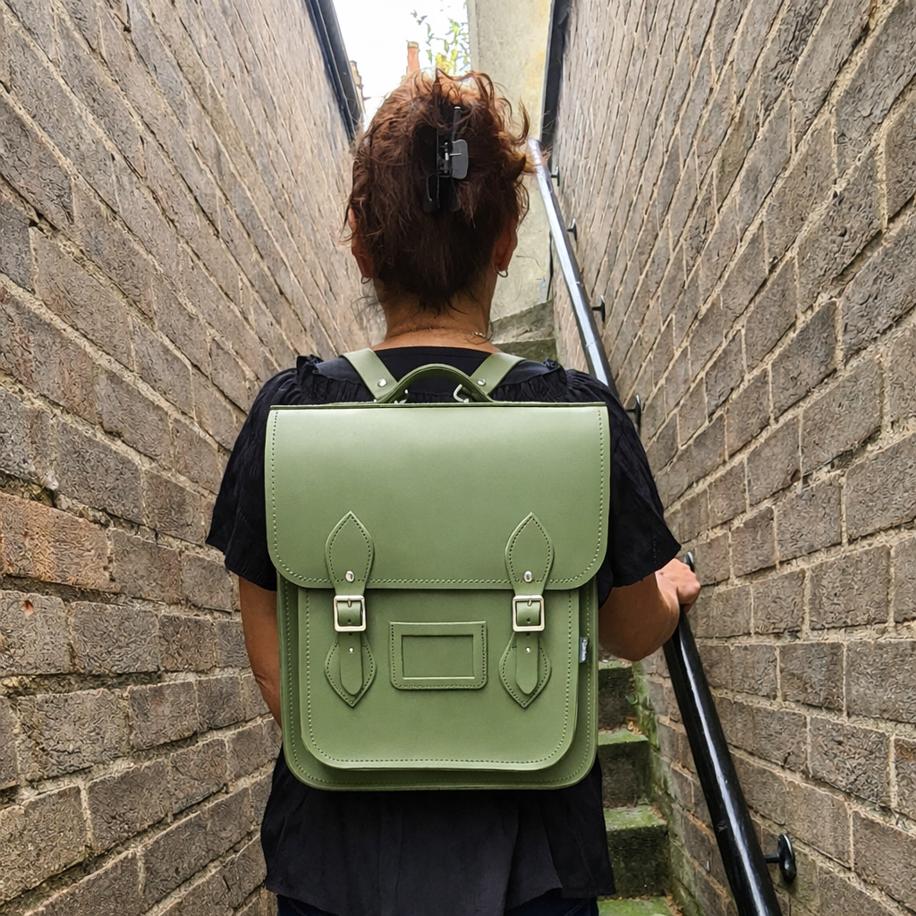 Person wearing the Zatchels Handmade Leather City Backpack in Sage Green on a city street, showing the Plus size worn as a crossbody bag