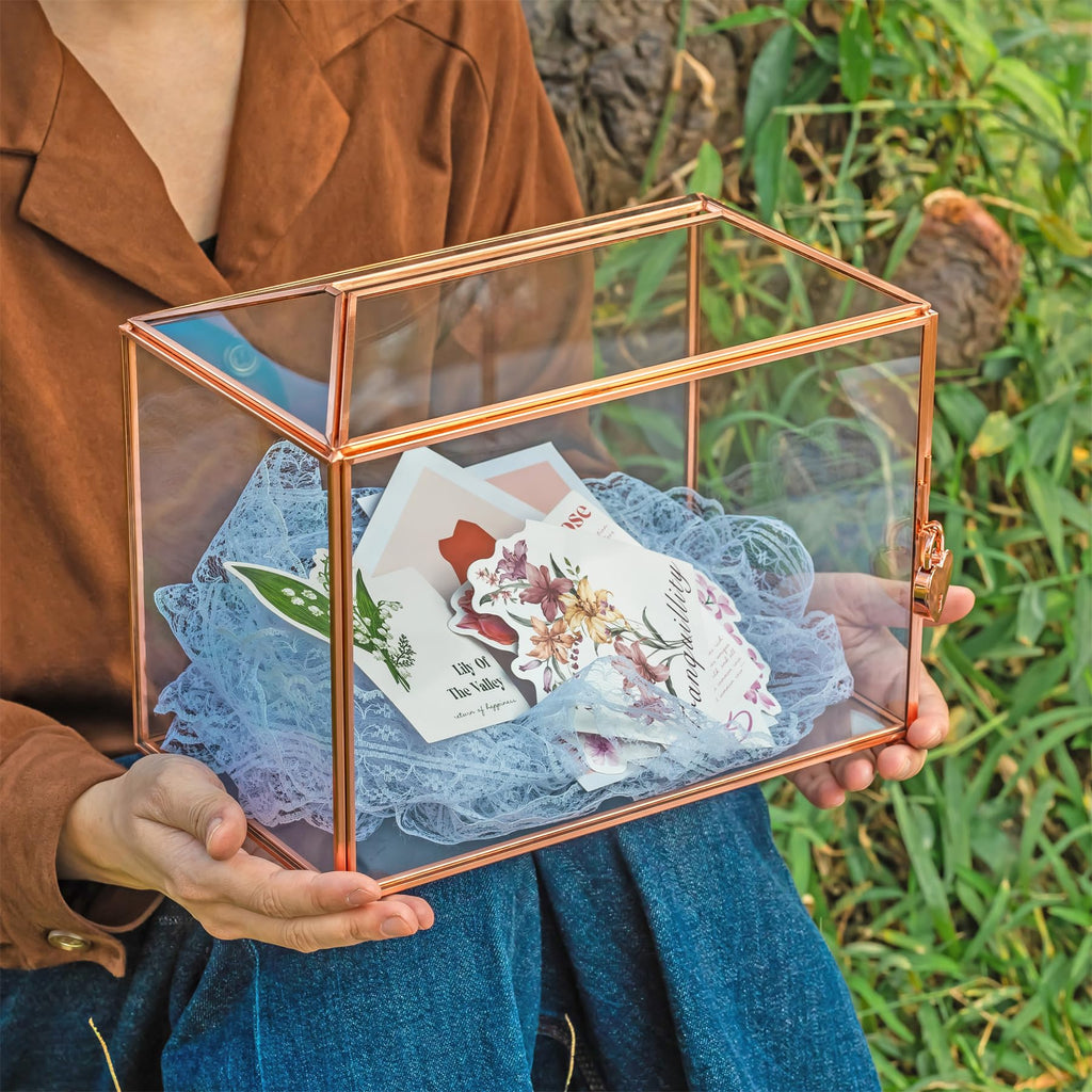 Person holding a glass box with floral cards and lace fabric outdoors.